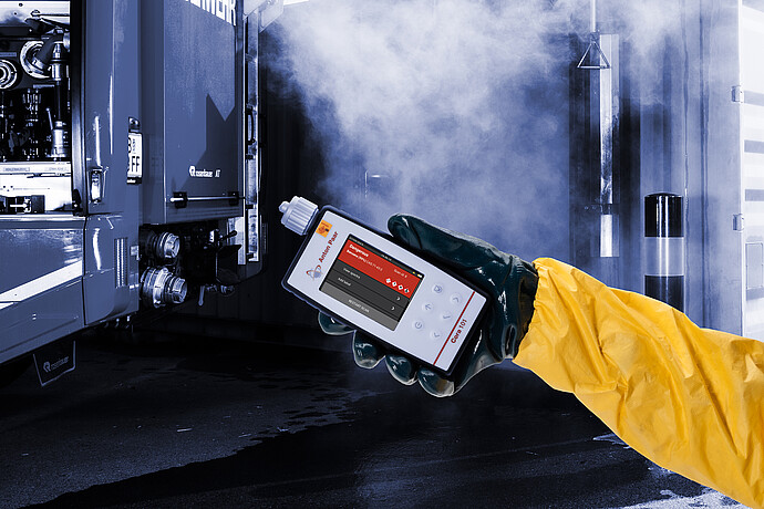 Person in hazmat suit using the Anton Paar Cora 101 handheld Raman spectrometer near a container in a smoky emergency response setting.