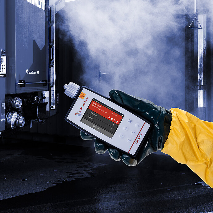 Person in hazmat suit using the Anton Paar Cora 101 handheld Raman spectrometer near a container in a smoky emergency response setting.