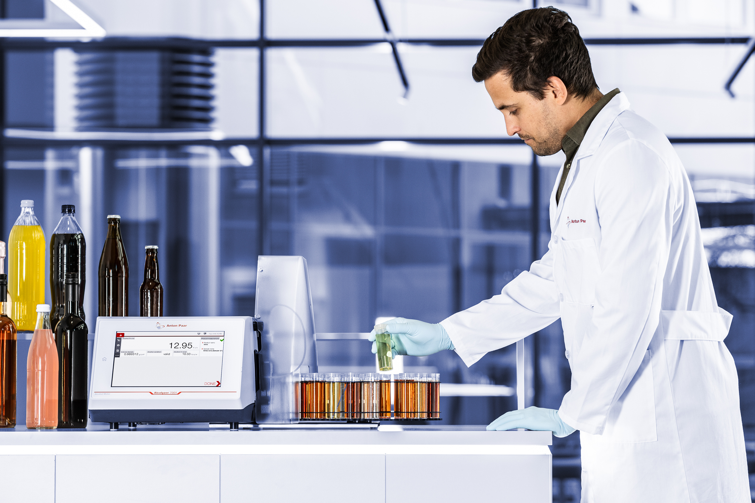 Technician in lab coat operating an Anton Paar Alcolyzer 7001 Beer with beer samples in test tubes and various beverage bottles.