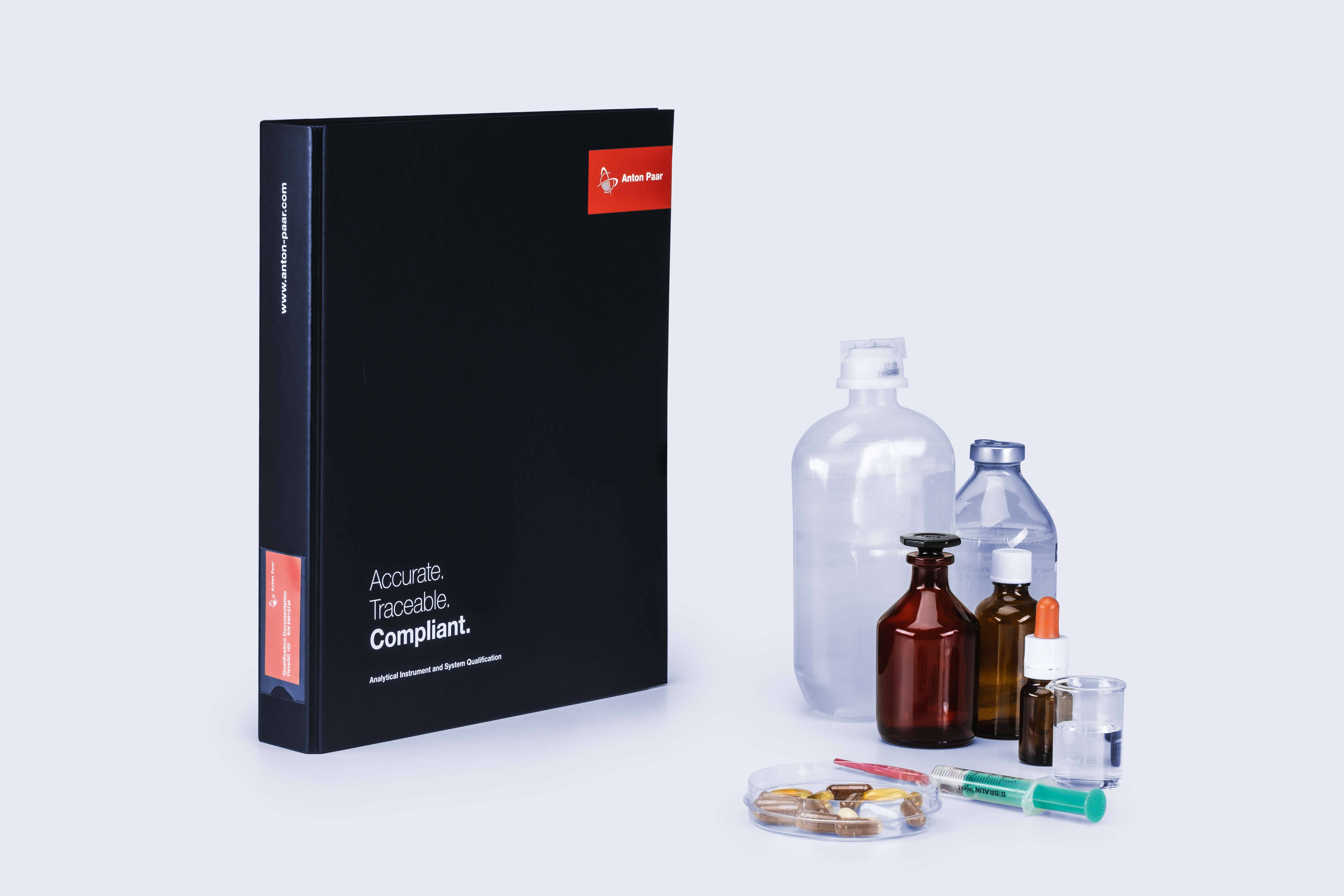 Black Anton Paar qualification binder next to assorted pharmaceutical packaging including vials, ampoules, droppers, and blister packs.